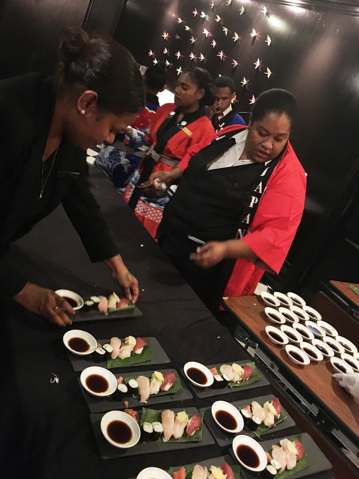 Papua New Guinean waitresses serving Sushi (Origami paper cranes on the wall in the back)